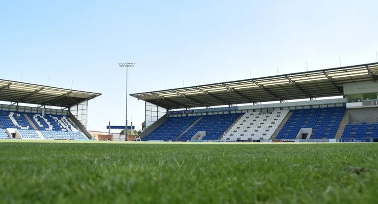 Hình ảnh cận cảnh khu vực đường pitch tại JobServe Community Stadium, cho thấy băng ghế dự bị và đường biên sân bóng đá Anh của Colchester United.